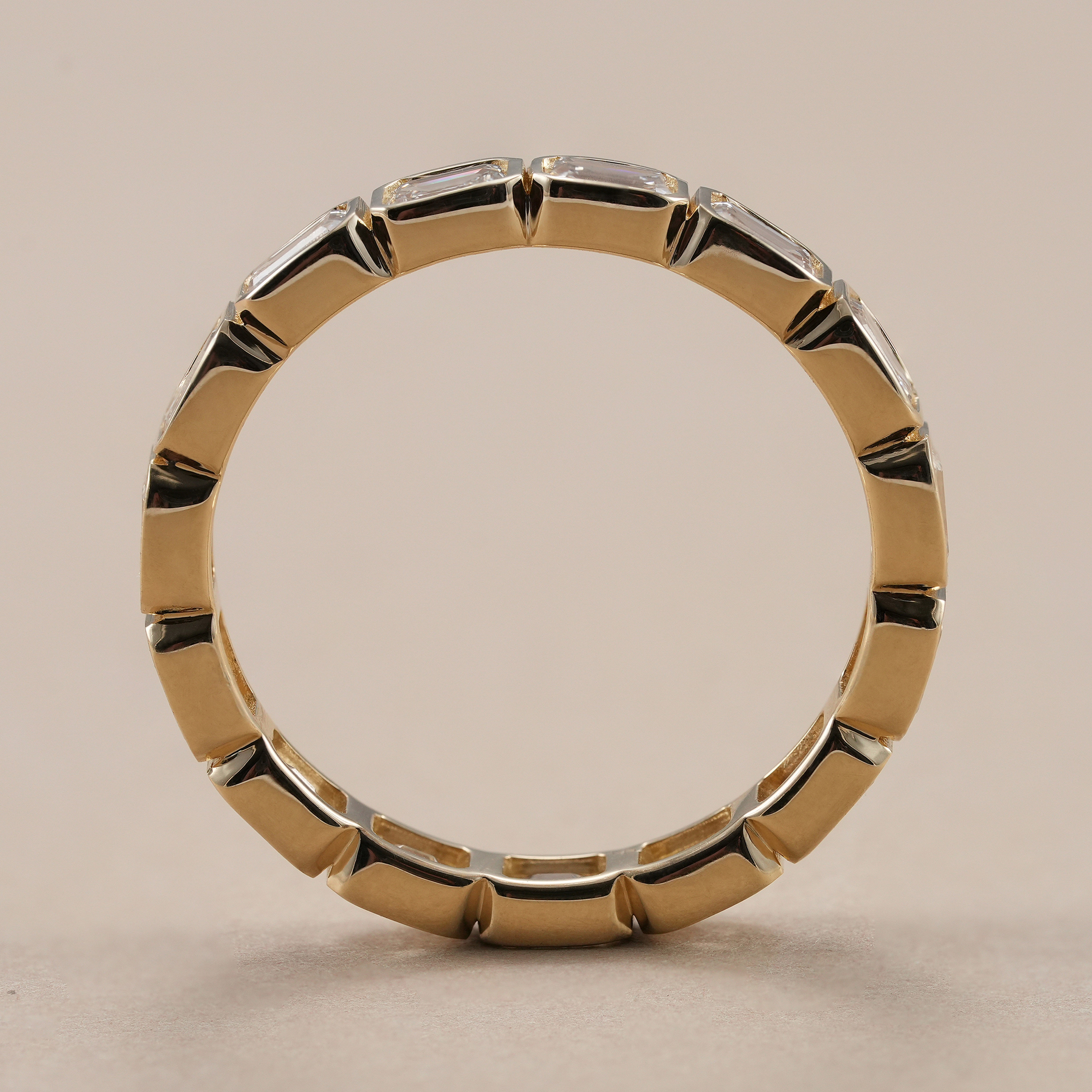 Bezel set emerald diamond eternity wedding band with polished finish.