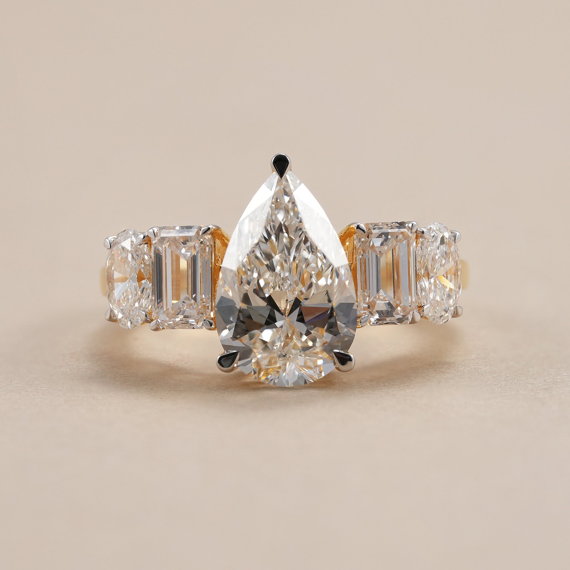 Pear lab grown diamond engagement ring with emerald and oval side stones.