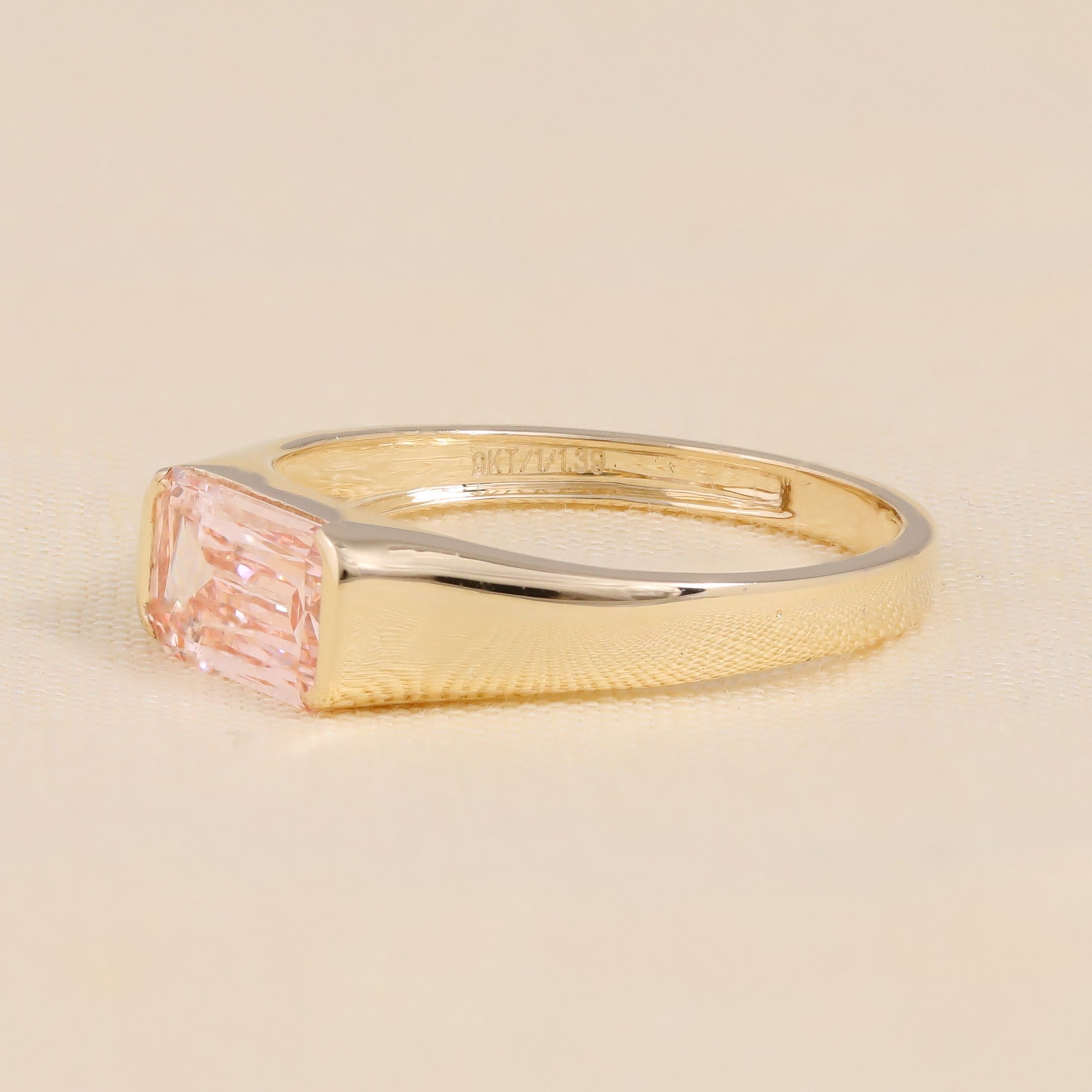Gold bezel set ring featuring emerald cut pink lab created diamond.