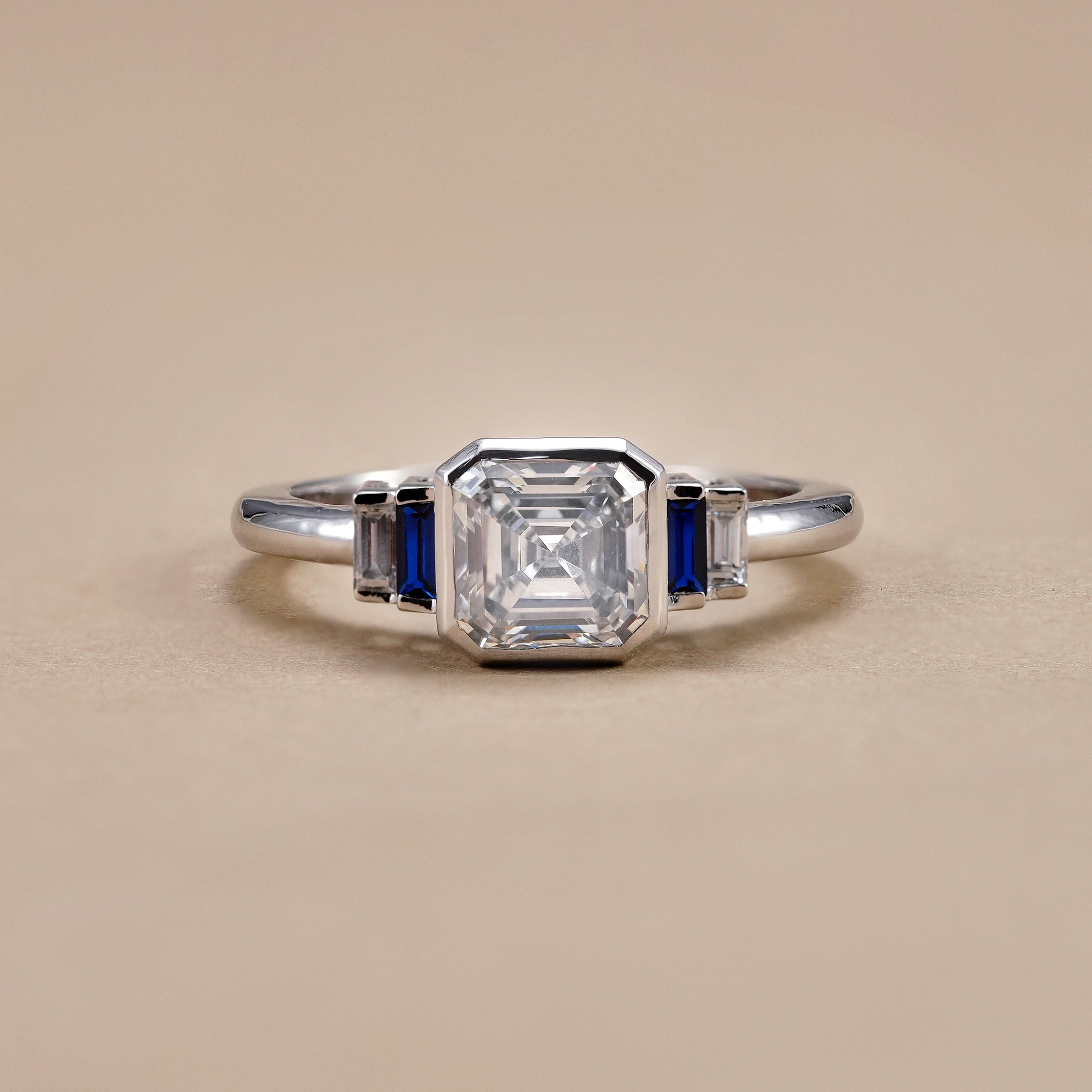 Bezel set Asscher cut lab diamond engagement ring with blue sapphire baguette side stones.
