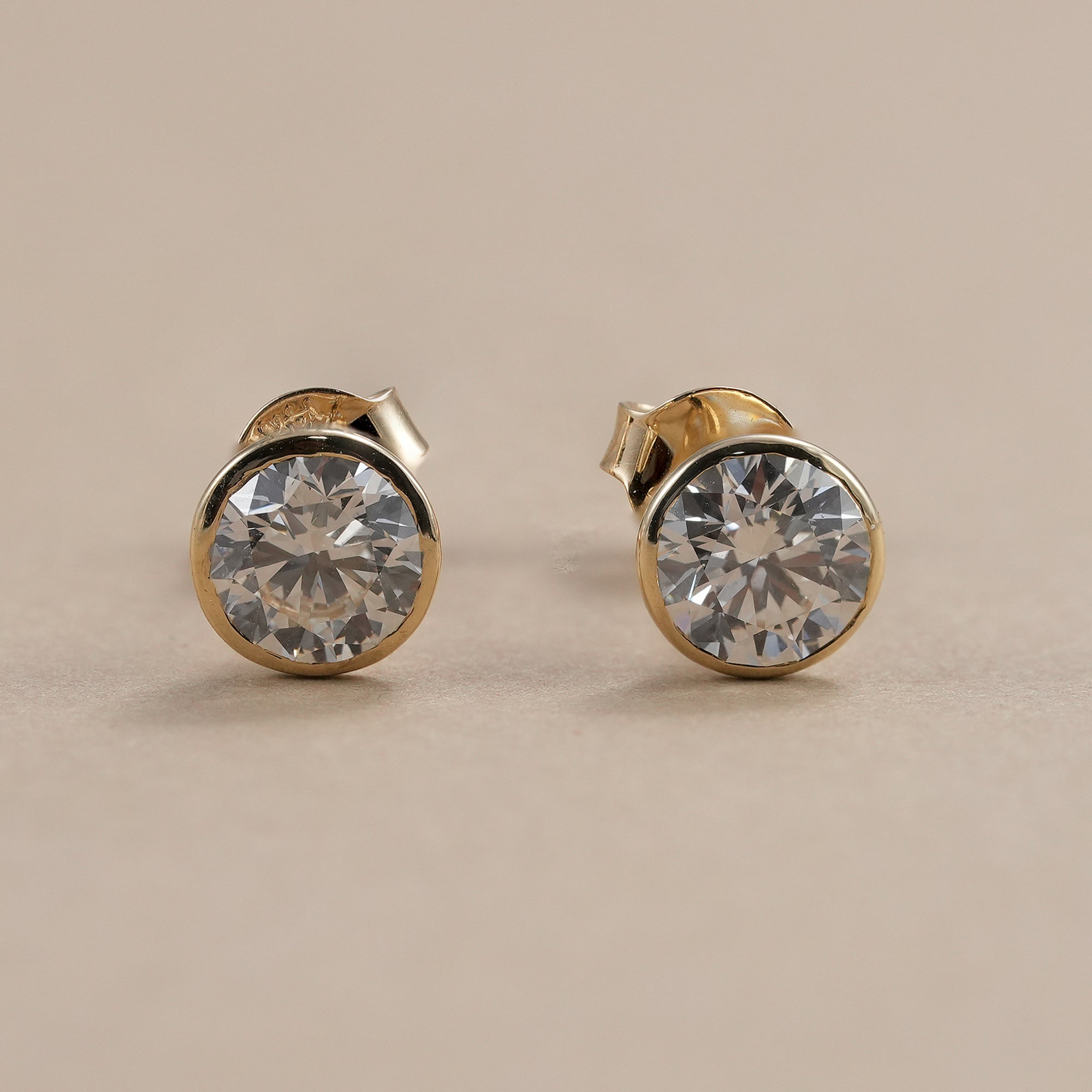 Bezel set round lab grown diamond stud earrings in yellow gold.