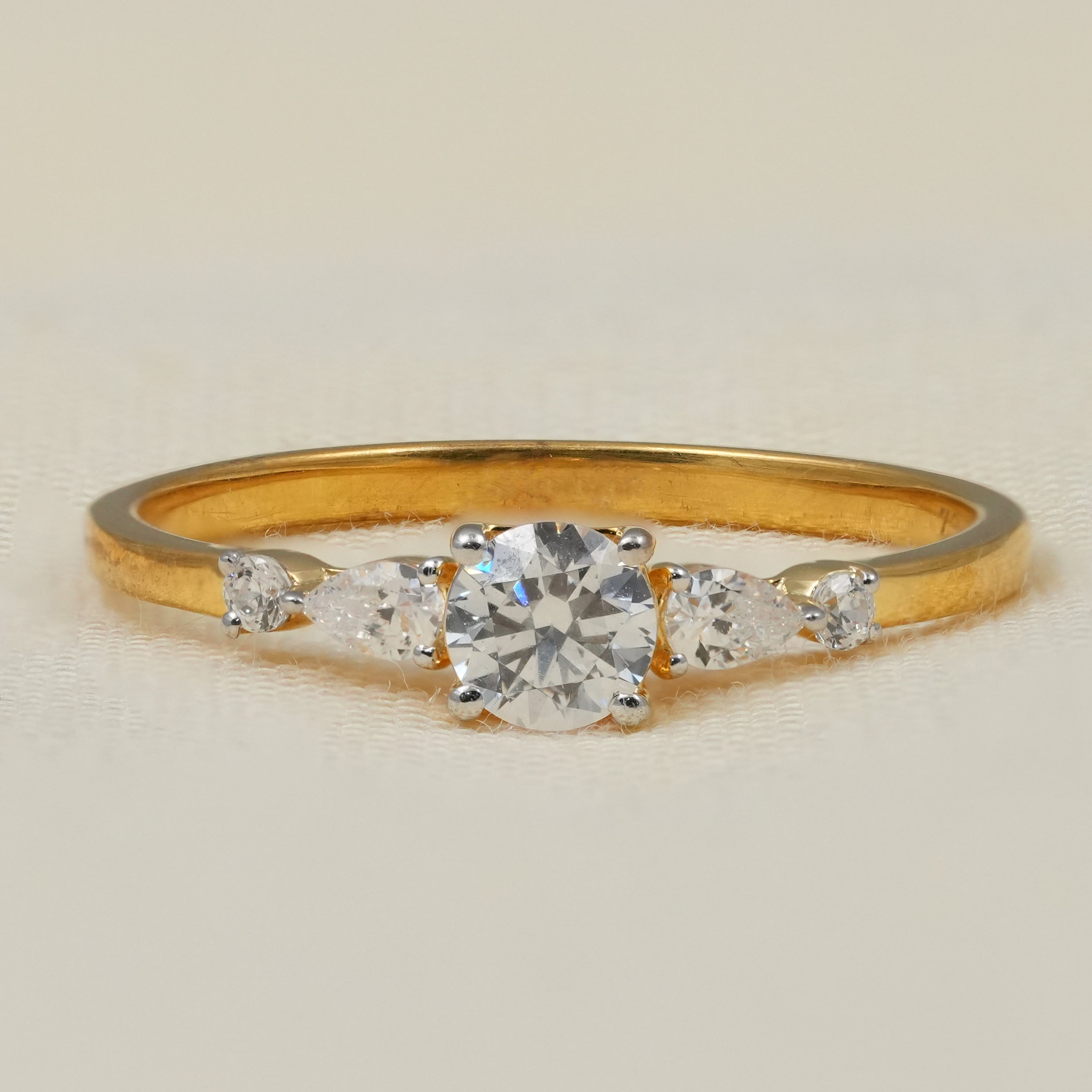 Delicate round lab grown diamond engagement ring with pear side stones in yellow gold