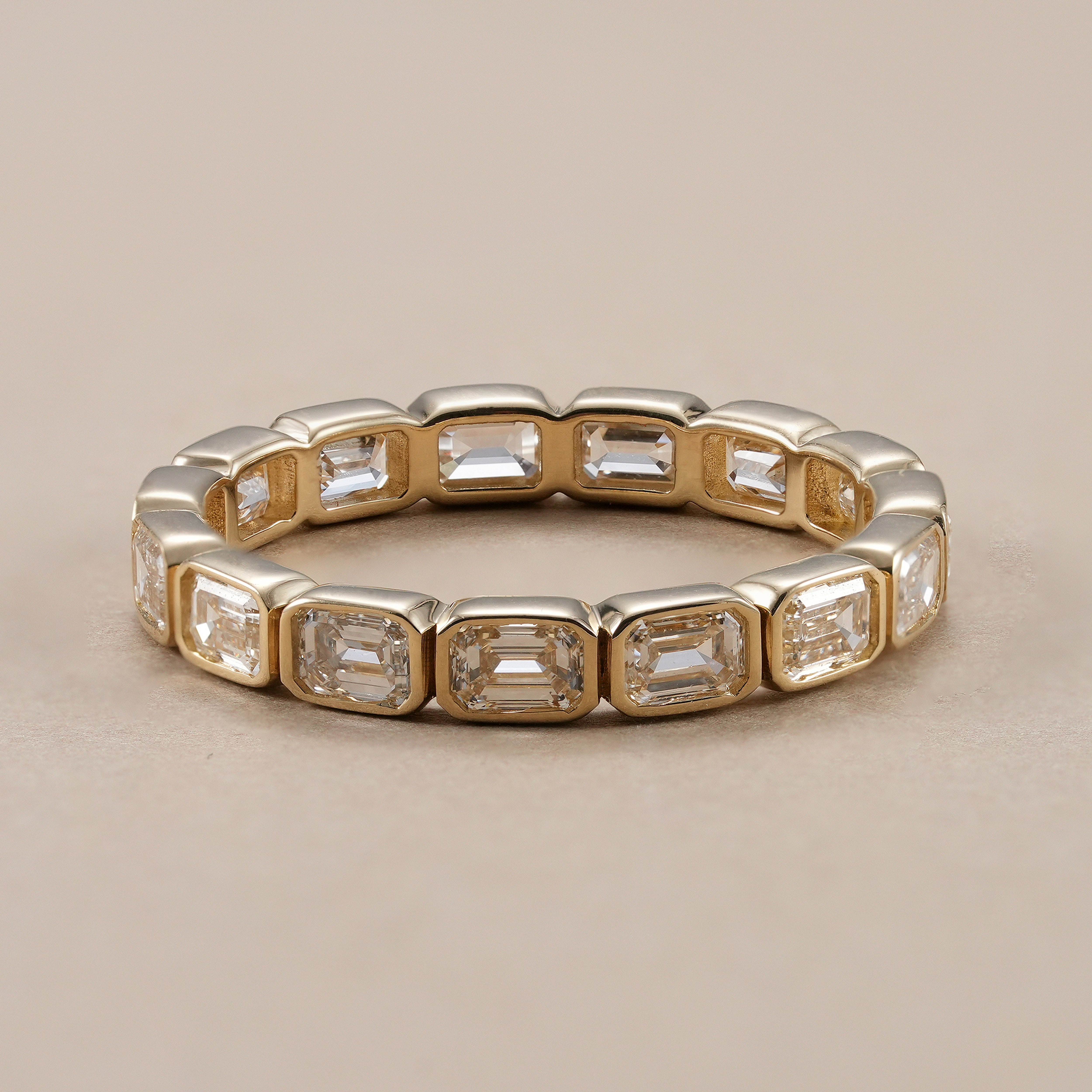 Emerald cut bezel set lab grown diamond eternity ring in yellow gold.
