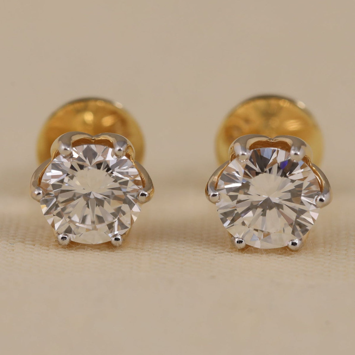 Gold stud earrings with clear gemstones on a beige background
