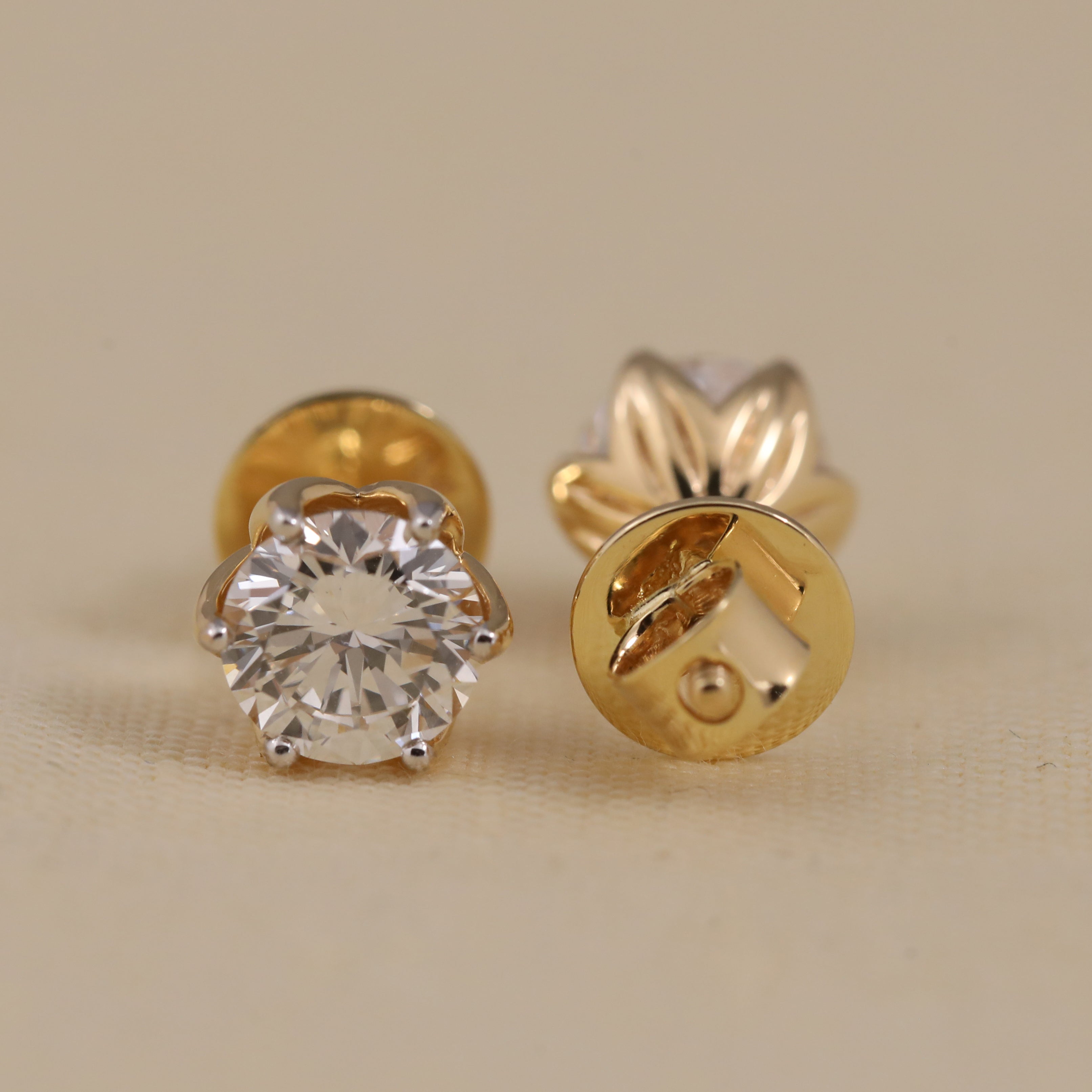 Gold stud earrings with a clear gemstone on a beige background