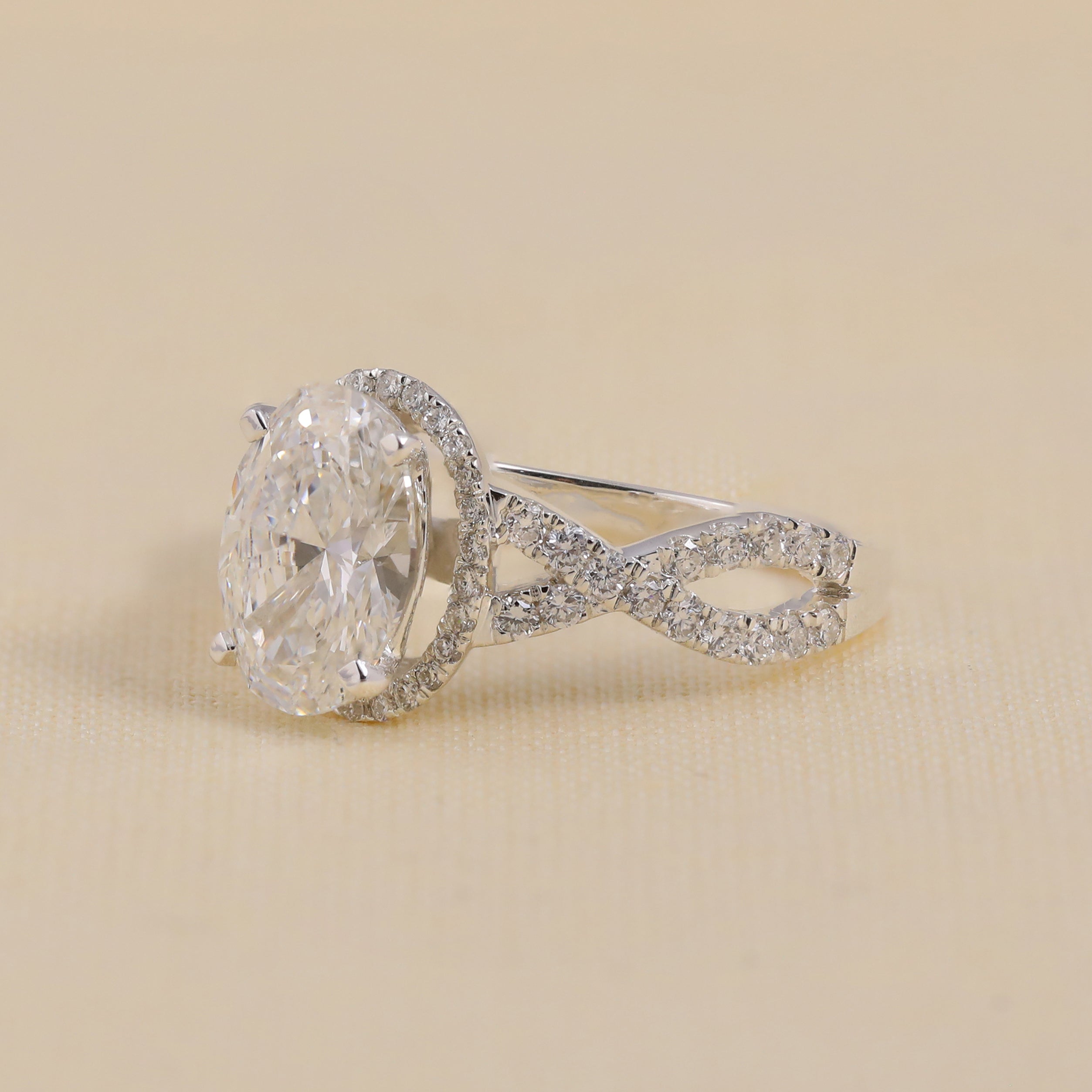 White gold ring with an oval center diamond and a crisscross pavé band.